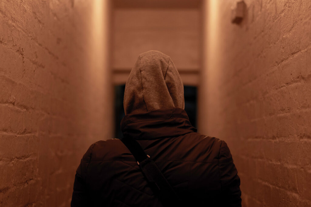 a person in a hood thinking of the effects of fentanyl addiction walks down a dimly lit hallway