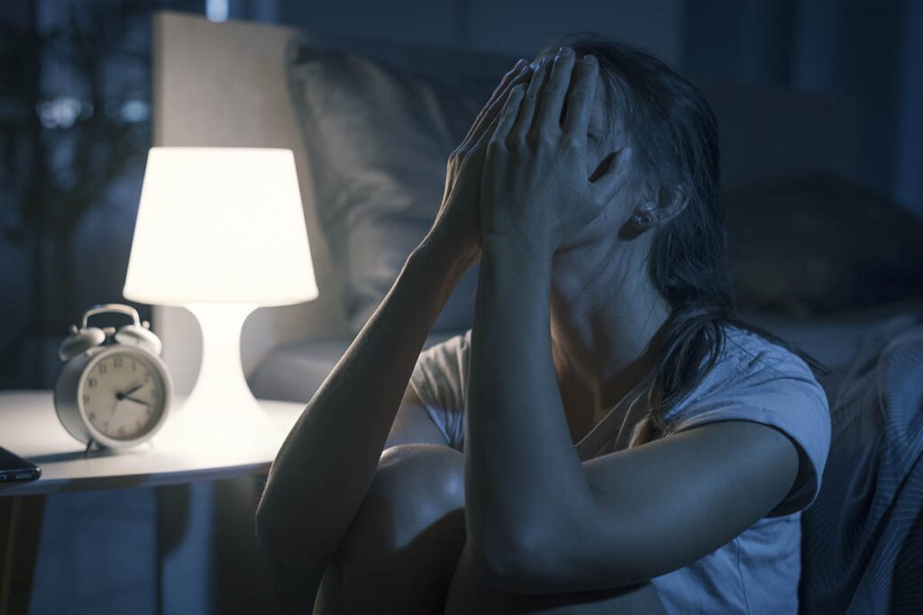 a person struggling with symptoms of meth addiction sits on a floor holding their head